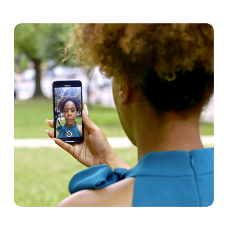 This image shows a woman speaking taking a selfie video on her phone, representing communication opportunities built into fundraising software.